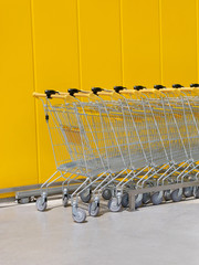 Stack of new shiny shopping carts in a supermarket with yellow wall in background