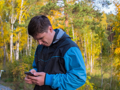 The guy tilted his head and looks at the smartphone screen. Passion for games while walking. Autumn landscape