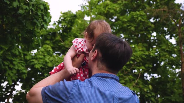 Dad is holding small daughter in summer park. Dad plays with small child, tosses up baby is happy and laughs. Slow motion.