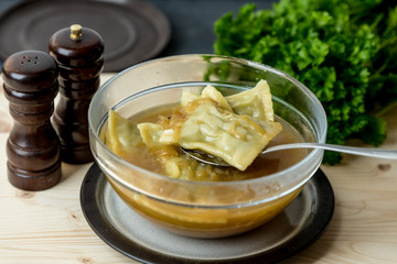 maultaschen, German, traditional dumplings in a bowl with onion soup, next to fresh parsley, salt shaker and pepper pot