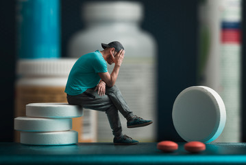 The man sitting on the pills. He's depressed. Flacons of medicines in the background - obrazy, fototapety, plakaty