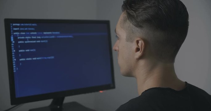 young man programmer writing code while working at computer in office