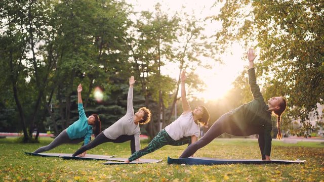 Good-looking women in sports clothing are doing yoga exercises in park on sunny day in autumn enjoying practice and nature. Youth and sports concept.
