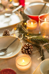 christmas, holidays and decoration concept - table served and decorated for festive dinner with candles, pine cones and fir branch