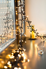 holidays and decoration concept - close up of christmas garland glowing on window sill