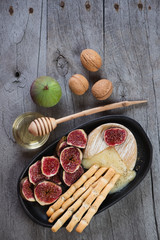 Melted camembert served with grissini, slices of fig fruits and honey. Above view on a grey rustic wooden table, vertical shot