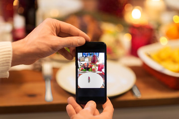 technology, eating and holidays concept - close up of male hands photographing food by smartphone at christmas dinner
