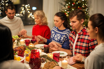 holidays and celebration concept - friends holding hands and praying while having christmas dinner at home