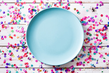 Colorful confetti and blue plate on white wooden background. Top view

