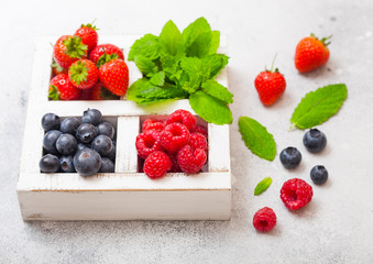 Fresh raw organic berries in white vintage wooden box on kitchen table background. Top view. Strawberry, Raspberry, Blueberry and Mint leaf