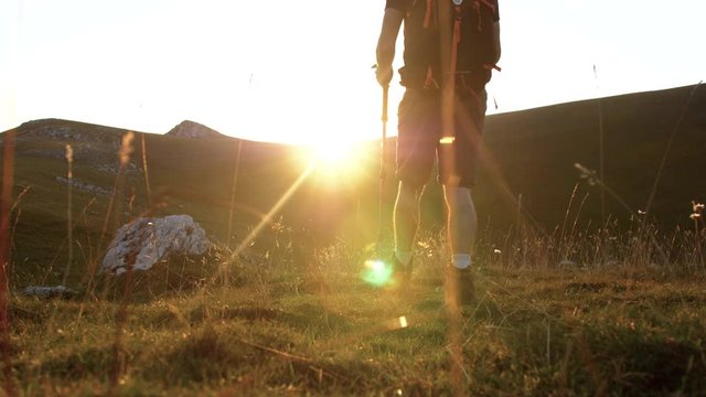 Young trekker man walking on the mountain towards sunset with backpack, boots and trekking poles. Low angle shot. Abruzzo Italy.