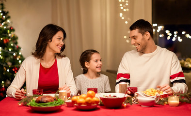 holidays, family and celebration concept - happy mother, father and little daughter having christmas dinner at home