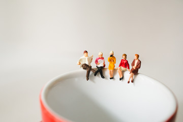 Miniature people  sitting on cup of coffee using as business meeting and social concept - obrazy, fototapety, plakaty