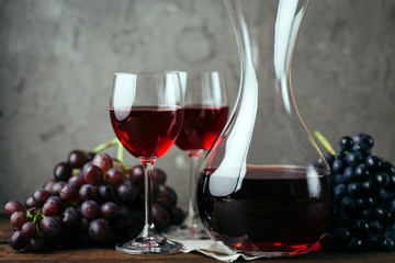 Red wine, decanter, two glasses and a bunch of grapes on a gray background
