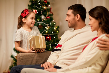 holidays, family and celebration concept - happy mother, father and little daughter with christmas present at home