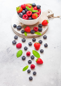 Fresh raw organic berries isolated in white ceramic bowl plate on round wooden board. Top view. Strawberry, Raspberry, Blueberry and Mint leaf