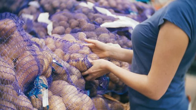 A woman in a supermarket buying vegetables, potatoes.