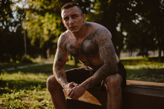 Shirtless tattooed man resting on the park bench