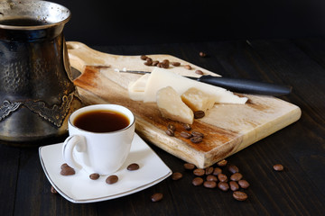 Cup of coffee and cheese on cutting board on dark background
