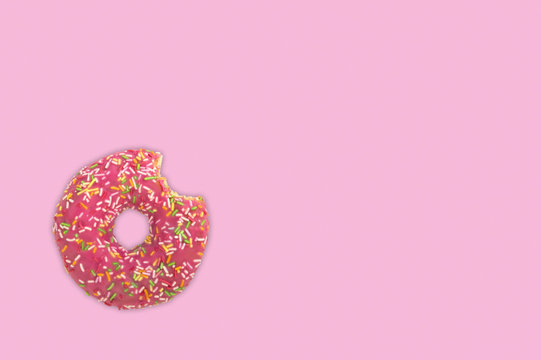 Bitten donut with colorful sprinkles over pink background.