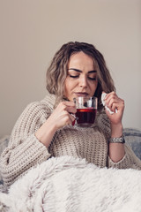 Sick Woman. Flu. Woman Caught Cold. Sitting on the Sofa. Headache. Virus. young girl covered in a blanket on a cold day enjoying a cup of tea.