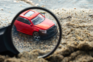 viewed through a magnifying glass red car on the wet sand near the pond
