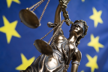 Fototapeta na wymiar Statue of the blindfolded goddess of justice Themis or Justitia, against an European flag, as a legal concept