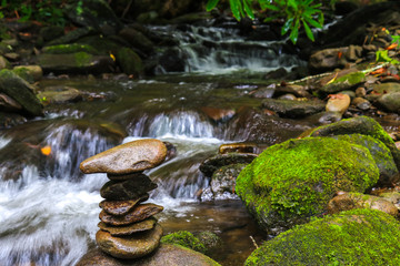 Stacked spa rocks with cascading water and mosey rocks in background; nature meditation concept 