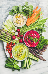 Healthy summer vegan snack plate. Flat-lay of Chickpea, beetroot, spinach hummus dips with fresh vegetables on grey marble background, top view. Clean eating, dieting, vegetarian party food concept