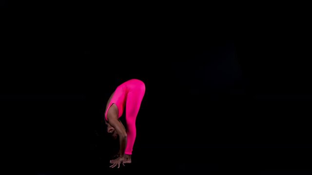 amazing female yoga instructor in bright pink clothing moving between poses against black background