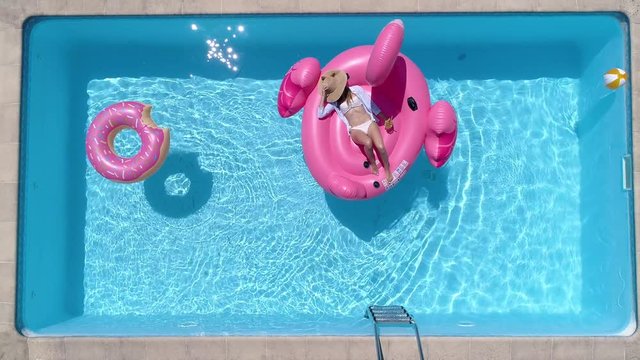 Aerial - Young woman relaxing on a giant pink flamingo float in the pool at home