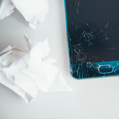 Smartphone with broken screen on white background with crumpled paper ball.