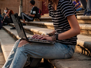 A teenage woman studying with a laptop on the stairs of a university in a university campus
