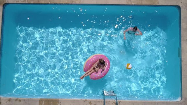 Aerial - Girl lying on donut pool float and tossing inflatable ball to her frien