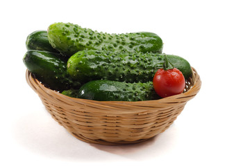 A small basket with small wet fresh cucumbers and one small tomato.