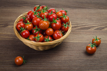 A small basket with small red tomatoes on a dark wooden table.