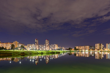 Fototapeta na wymiar Night cityscape of residential buildings and park with a pond in the urban outskirts