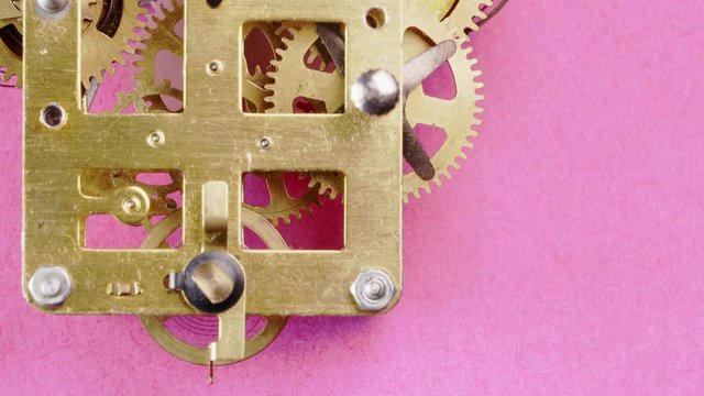 close up detail of running clock or watch machinnery on a pink background. Copy space available and suitable for time concepts as time goes by, Daylight saving time or growing old.