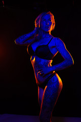 Muscled caucasian woman with tattoos and oiled skin poses under colored lights