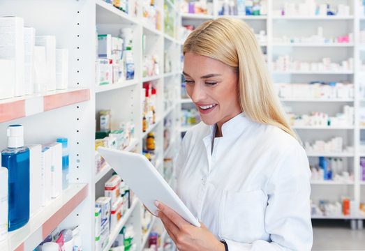 Cheerful pharmacist woman checking a medications on tablet at pharmacy drugstore