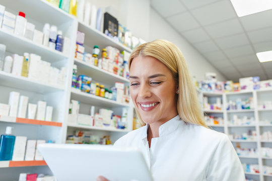 Cheerful pharmacist woman checking a medications on tablet at pharmacy drugstore