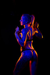 Fototapeta premium Muscled caucasian woman with tattoos and oiled skin poses under colored lights