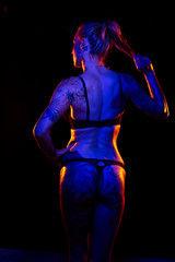 Fototapeta na wymiar Muscled caucasian woman with tattoos and oiled skin poses under colored lights