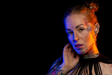 Muscled caucasian woman with tattoos and oiled skin wearing necklace and fishnet underwear poses under colored lights