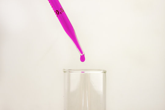 Purple chemical liquid in a flask with pipette pouring drops