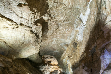 Dark cave view from inside with a lumen. Stalactites and stalagmites inside the stone grotto. Colorful stones in the cave. Lighting electricity beauty of the cave.