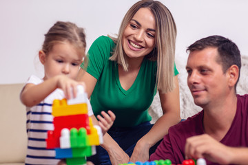 couple mother and father playing with little daughter cubes together at home.