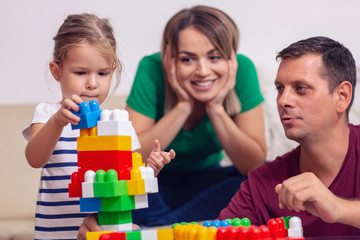 happy mother and father playing with daughter cubes together at home.