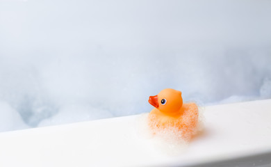 Orange playful rubber duck in a bubble bath, light blue background with bubbles. Kids spa concept....