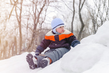 Fototapeta na wymiar A gloomy three-year-old boy sits on a snow hill